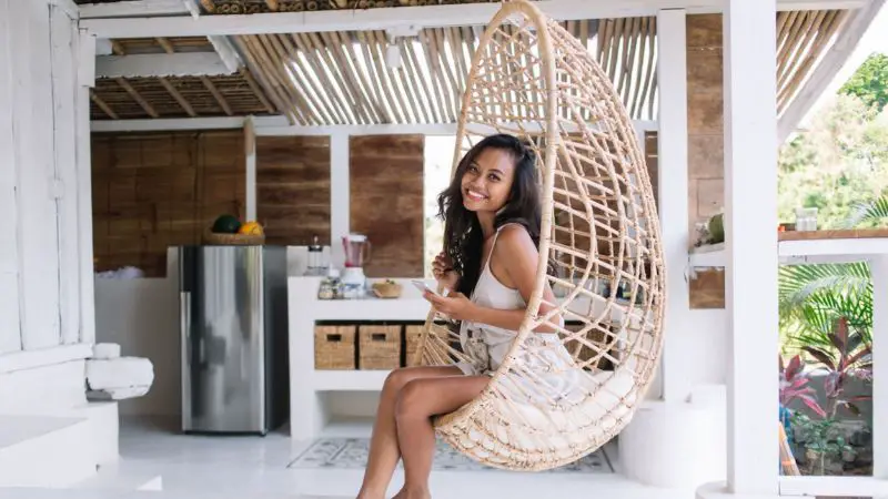 Happy woman sitting in wicker hanging egg chair